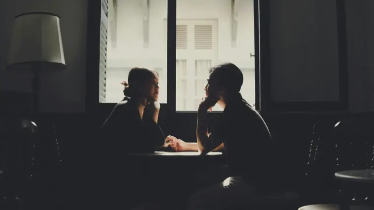 Two people talking across a table, silhouetted against a bright window