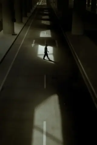 A lone figure crossing a dark corridor lit by one doorway