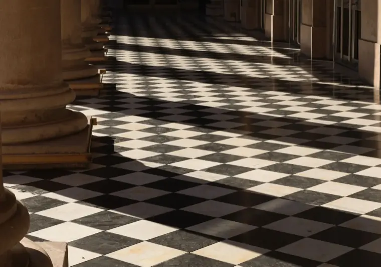 A sunlit stone corridor with a checkerboard floor and long shadows