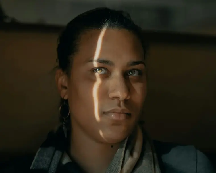 A face half-lit by a hard blade of window light in a dark room
