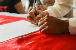 Hands signing a document resting on a red folder